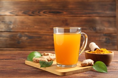 Photo of Aromatic turmeric tea in glass mug, roots, powder and green leaves on wooden table, space for text