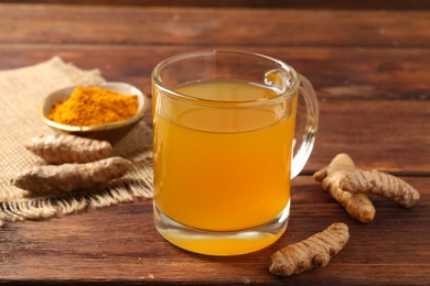 Photo of Aromatic turmeric tea in glass mug, roots and powder on wooden table, closeup