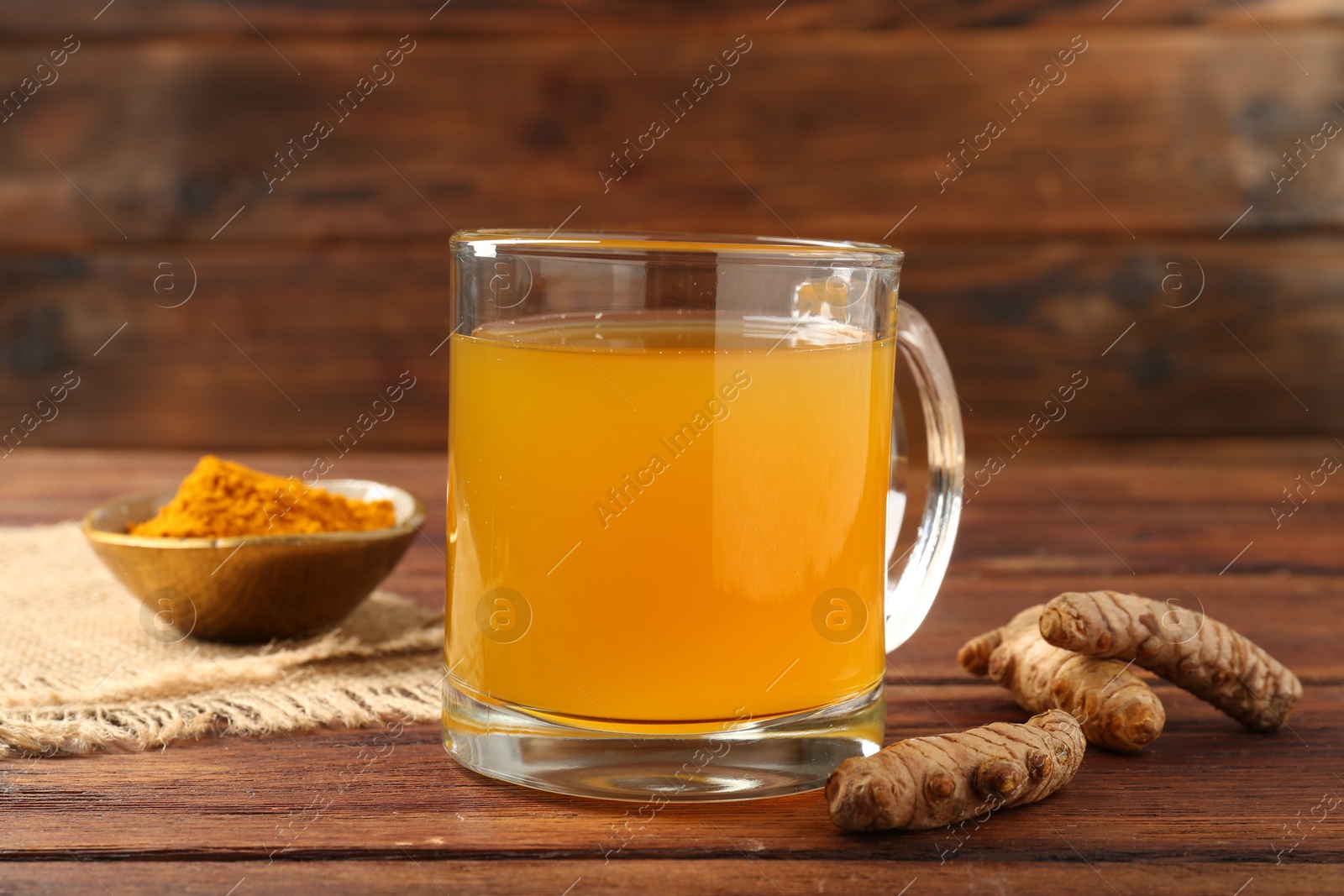 Photo of Aromatic turmeric tea in glass mug, roots and powder on wooden table, closeup