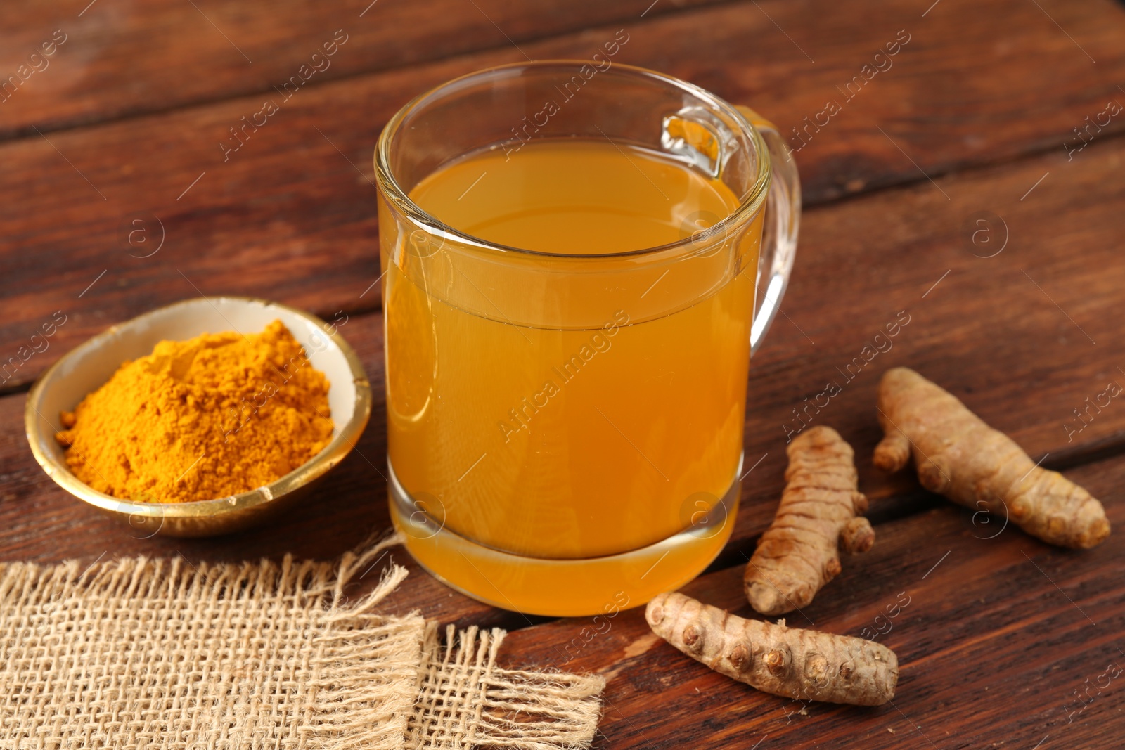 Photo of Aromatic turmeric tea in glass mug, roots and powder on wooden table, closeup