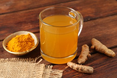 Photo of Aromatic turmeric tea in glass mug, roots and powder on wooden table, closeup