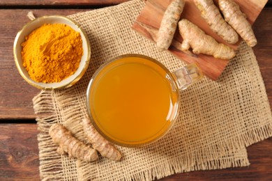 Photo of Aromatic turmeric tea in glass mug, roots and powder on wooden table, flat lay