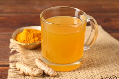 Photo of Aromatic turmeric tea in glass mug, roots and powder on table, closeup