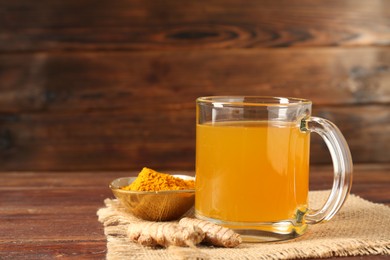 Photo of Aromatic turmeric tea in glass mug, roots and powder on wooden table, closeup. Space for text