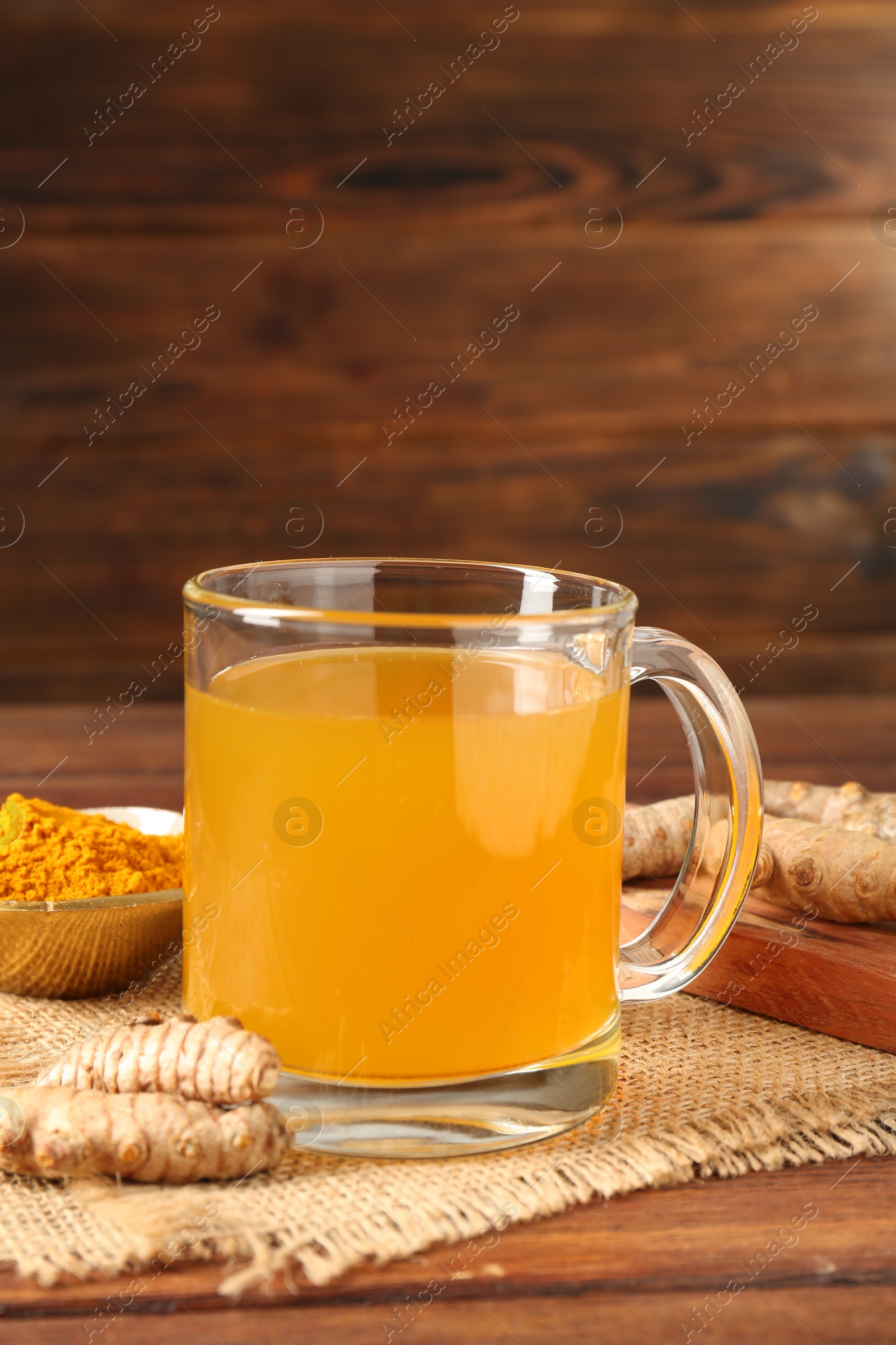 Photo of Aromatic turmeric tea in glass mug, roots and powder on wooden table