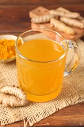 Photo of Aromatic turmeric tea in glass mug, roots and powder on wooden table, closeup