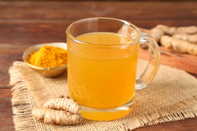 Photo of Aromatic turmeric tea in glass mug, roots and powder on wooden table, closeup