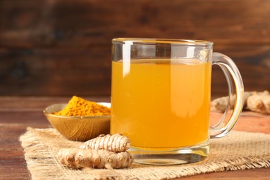 Photo of Aromatic turmeric tea in glass mug, roots and powder on wooden table, closeup