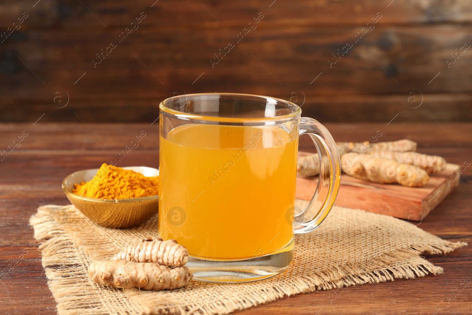 Photo of Aromatic turmeric tea in glass mug, roots and powder on wooden table