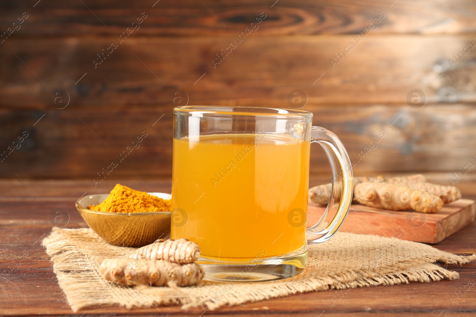 Photo of Aromatic turmeric tea in glass mug, roots and powder on wooden table