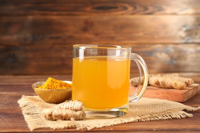 Photo of Aromatic turmeric tea in glass mug, roots and powder on wooden table