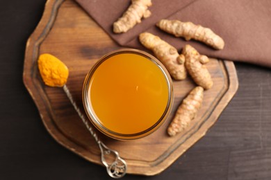 Photo of Aromatic turmeric tea in glass, roots and powder on wooden table, top view