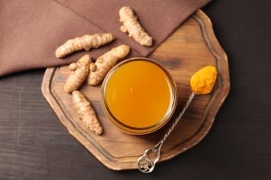 Photo of Aromatic turmeric tea in glass, roots and powder on wooden table, top view