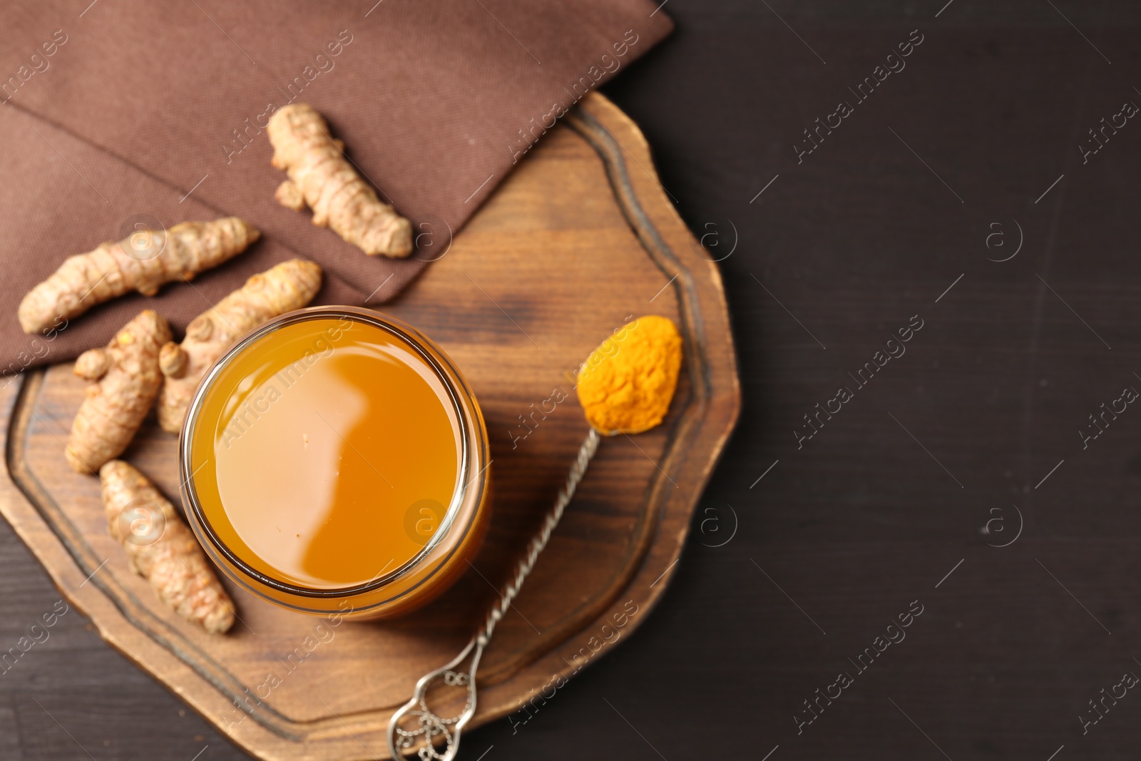 Photo of Aromatic turmeric tea in glass, roots and powder on wooden table, top view. Space for text