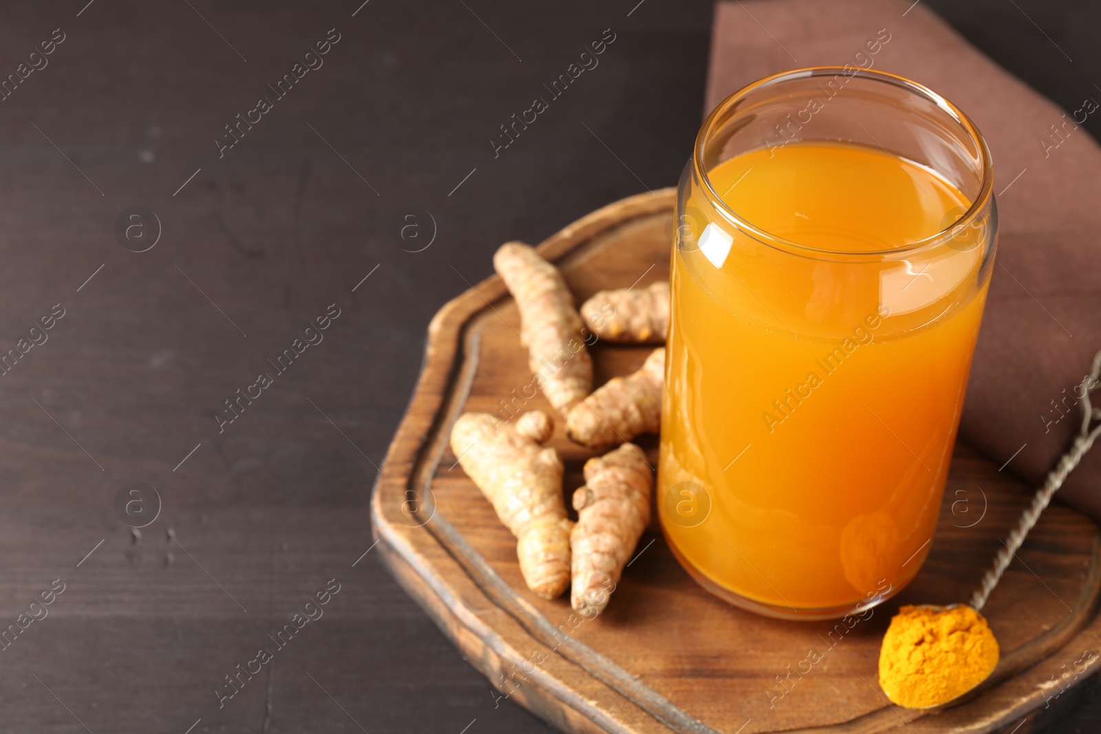 Photo of Aromatic turmeric tea in glass, roots and powder on wooden table, closeup. Space for text