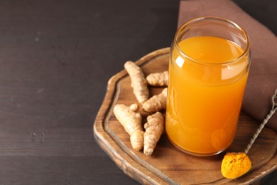 Photo of Aromatic turmeric tea in glass, roots and powder on wooden table, closeup. Space for text