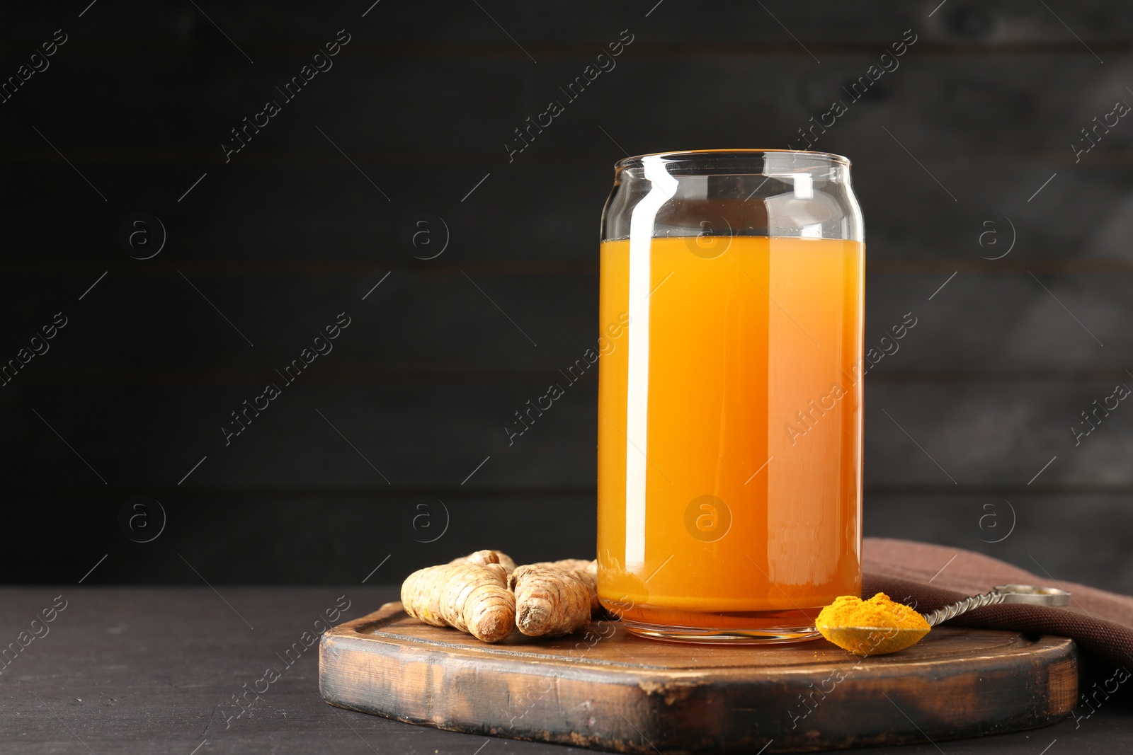 Photo of Aromatic turmeric tea in glass, roots and powder on wooden table, space for text