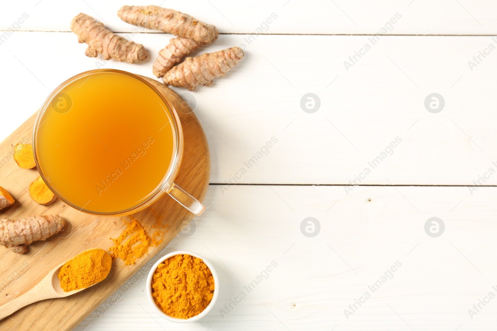 Photo of Aromatic turmeric tea in glass cup, roots and powder on white wooden table, flat lay. Space for text