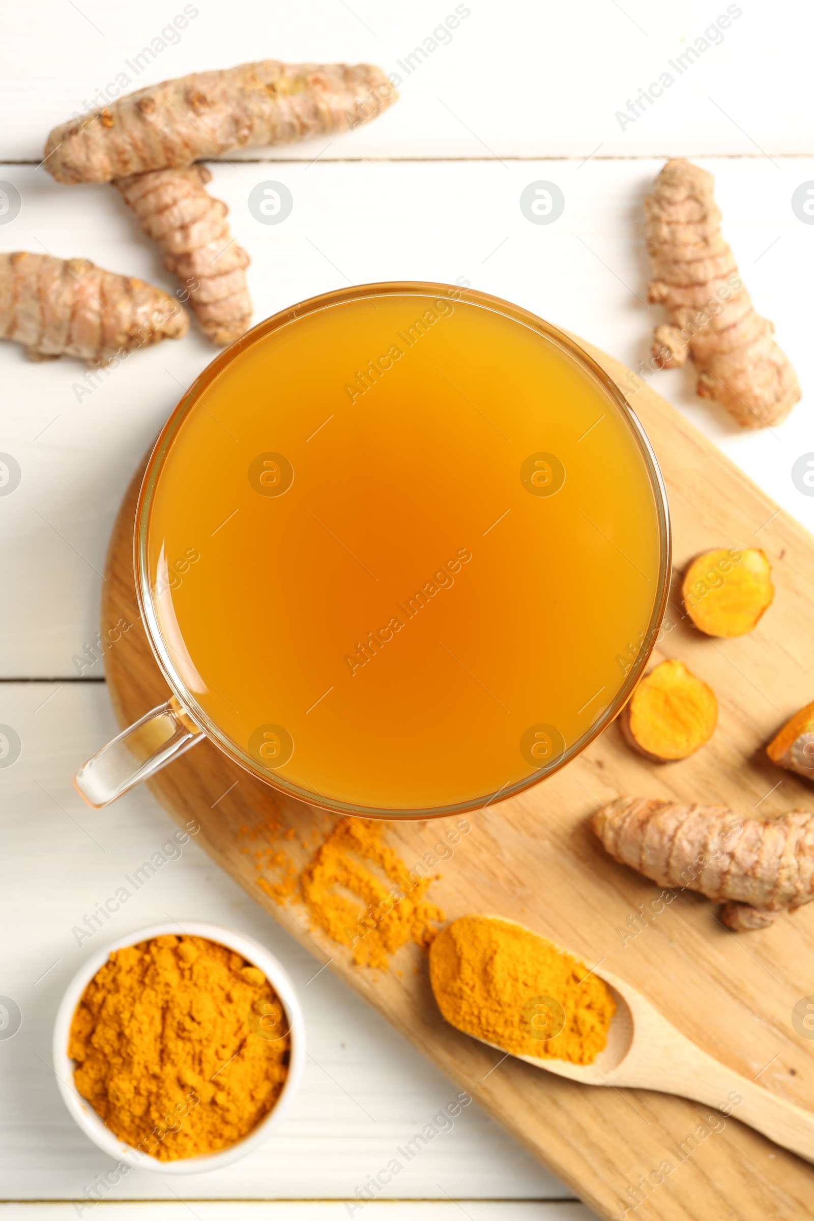 Photo of Aromatic turmeric tea in glass cup, roots and powder on white wooden table, flat lay