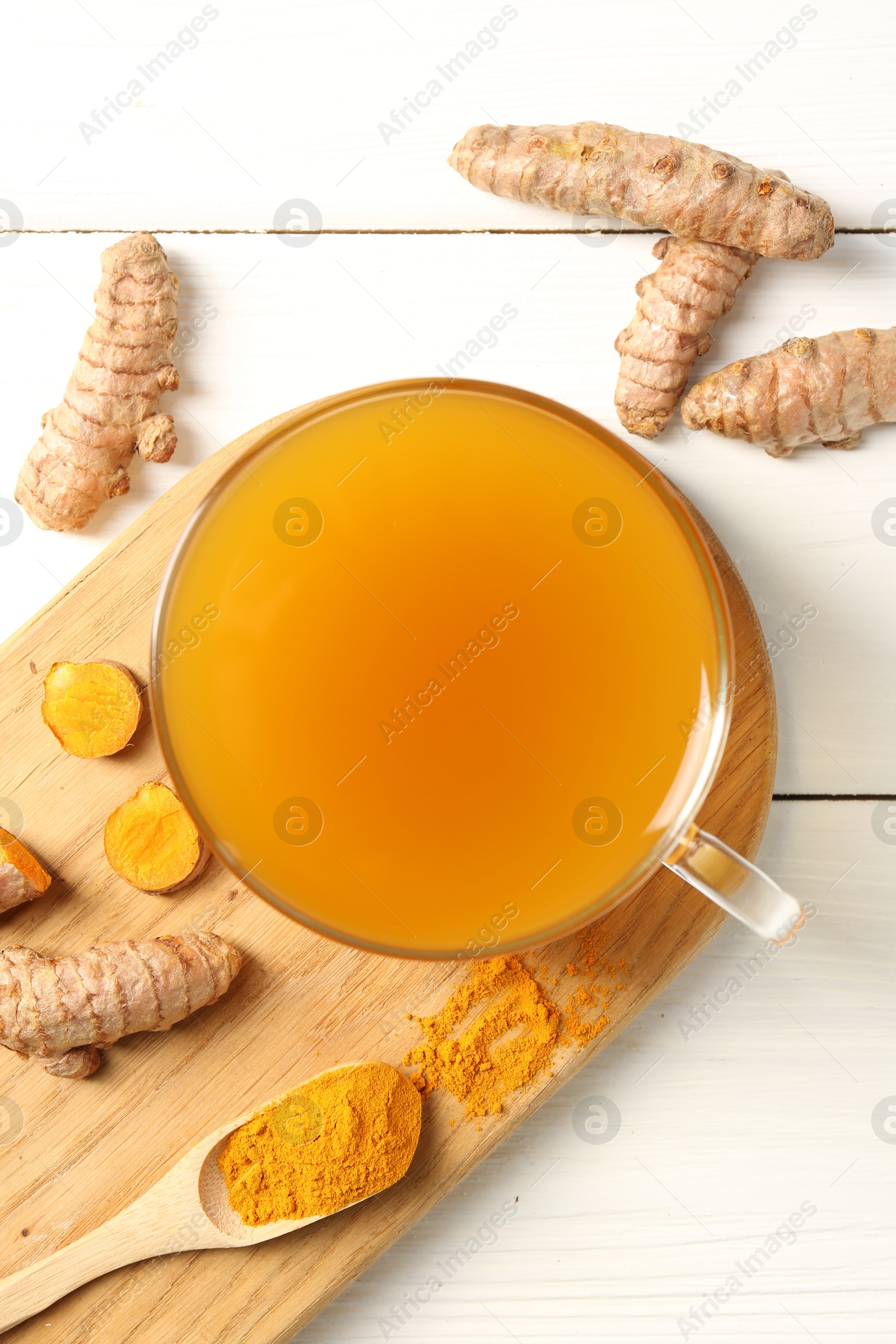 Photo of Aromatic turmeric tea in glass cup, roots and powder on white wooden table, flat lay