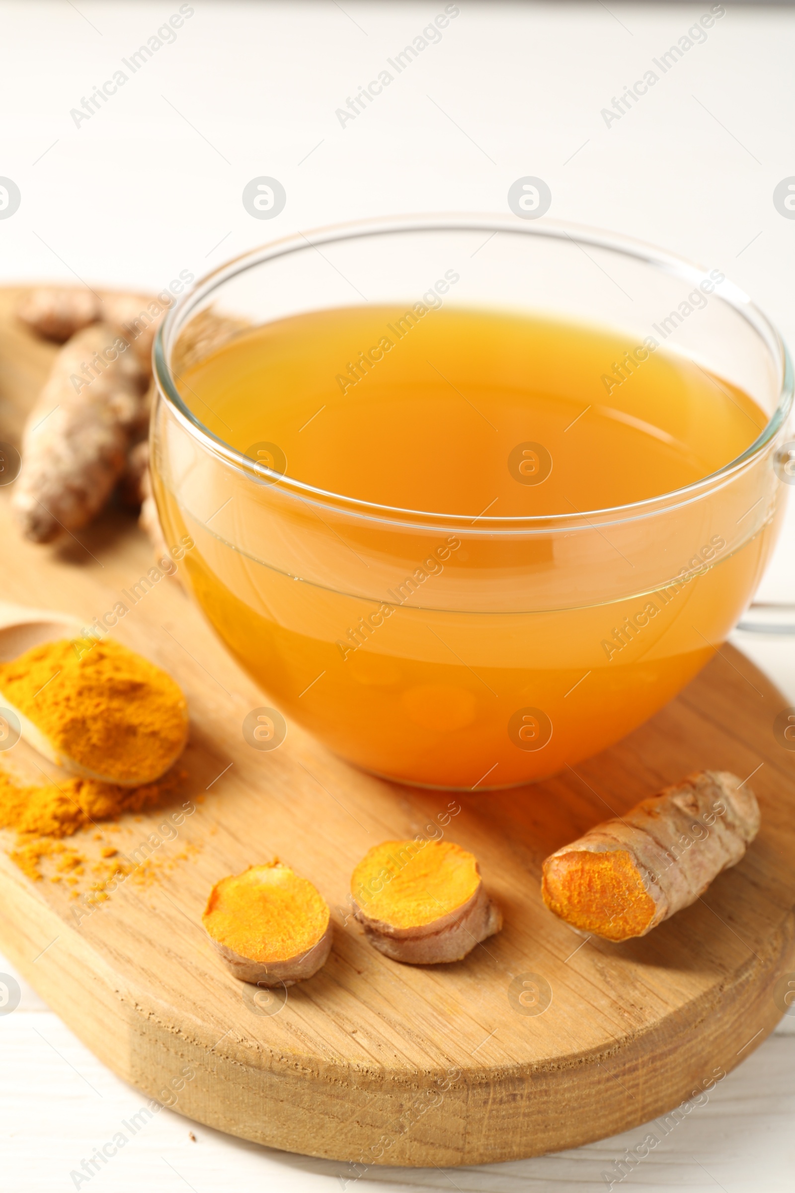 Photo of Aromatic turmeric tea in glass cup, roots and powder on white table, closeup