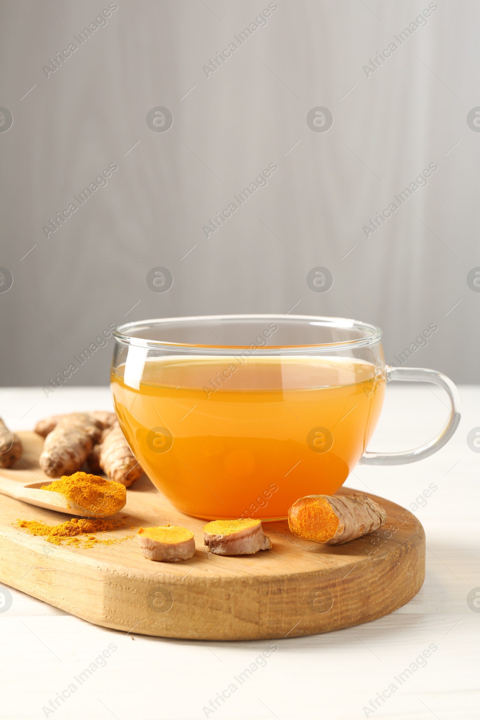 Photo of Aromatic turmeric tea in glass cup, roots and powder on white wooden table, closeup