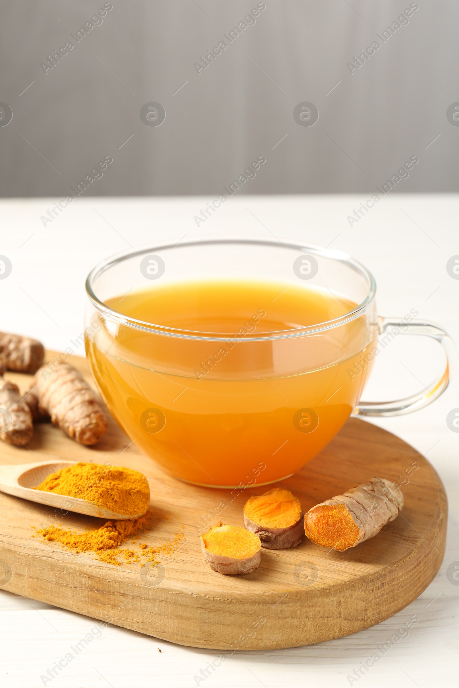 Photo of Aromatic turmeric tea in glass cup, roots and powder on white wooden table, closeup