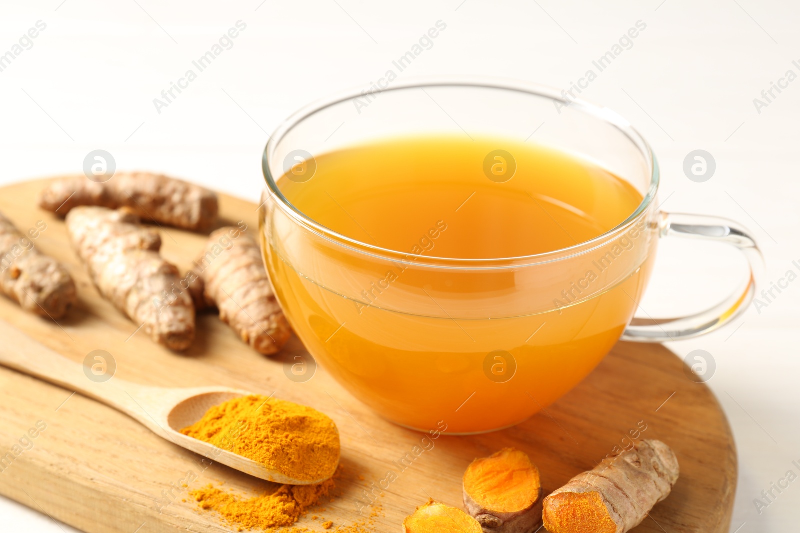 Photo of Aromatic turmeric tea in glass cup, roots and powder on white table, closeup