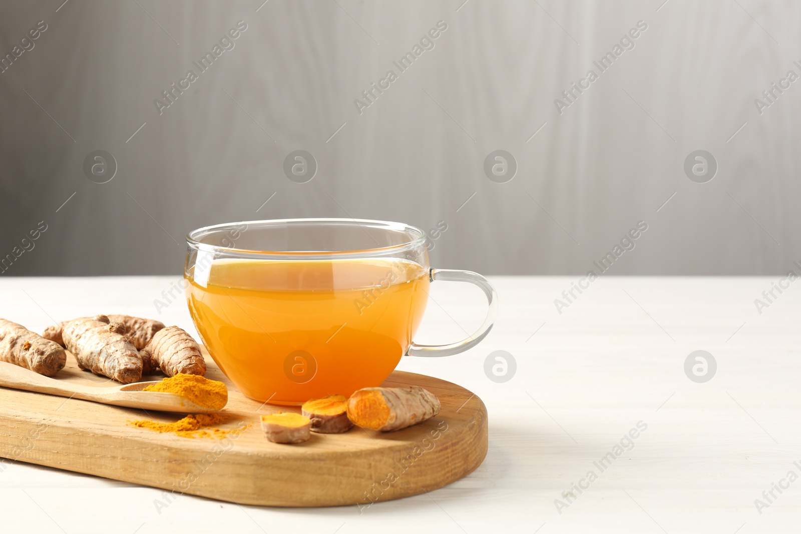 Photo of Aromatic turmeric tea in glass cup, roots and powder on white wooden table, closeup. Space for text