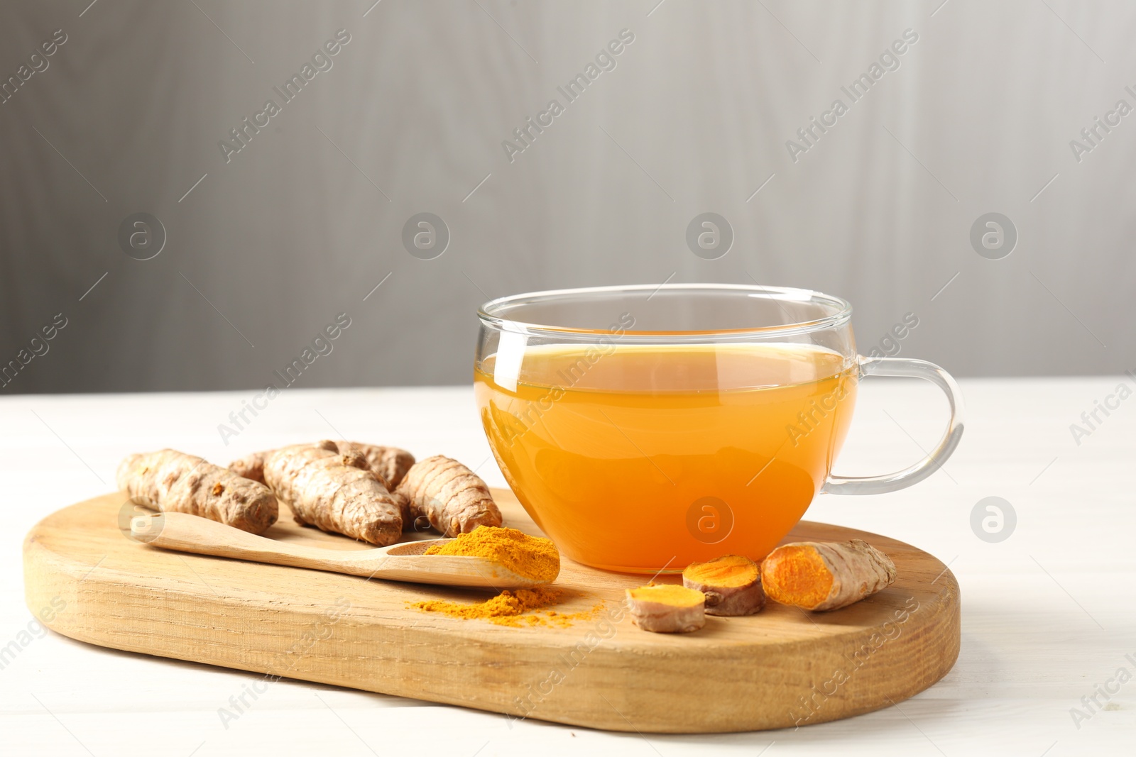 Photo of Aromatic turmeric tea in glass cup, roots and powder on white wooden table, closeup