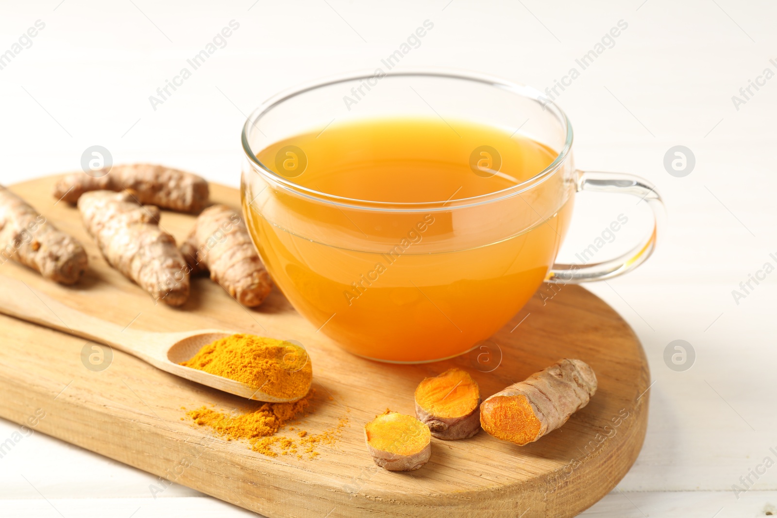 Photo of Aromatic turmeric tea in glass cup, roots and powder on white wooden table, closeup