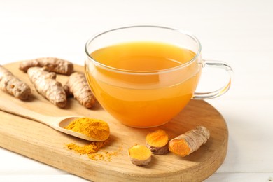 Photo of Aromatic turmeric tea in glass cup, roots and powder on white wooden table, closeup