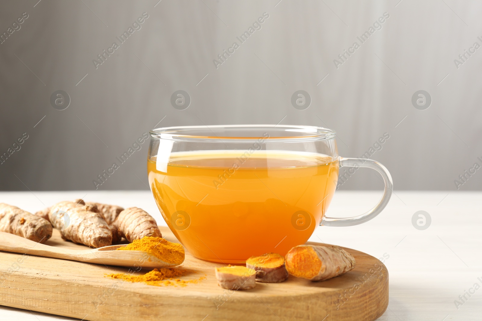 Photo of Aromatic turmeric tea in glass cup, roots and powder on white table, closeup