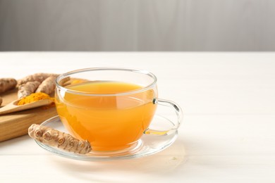 Photo of Aromatic turmeric tea in glass cup, roots and powder on white wooden table, closeup. Space for text