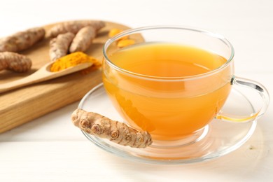 Photo of Aromatic turmeric tea in glass cup, roots and powder on white wooden table, closeup