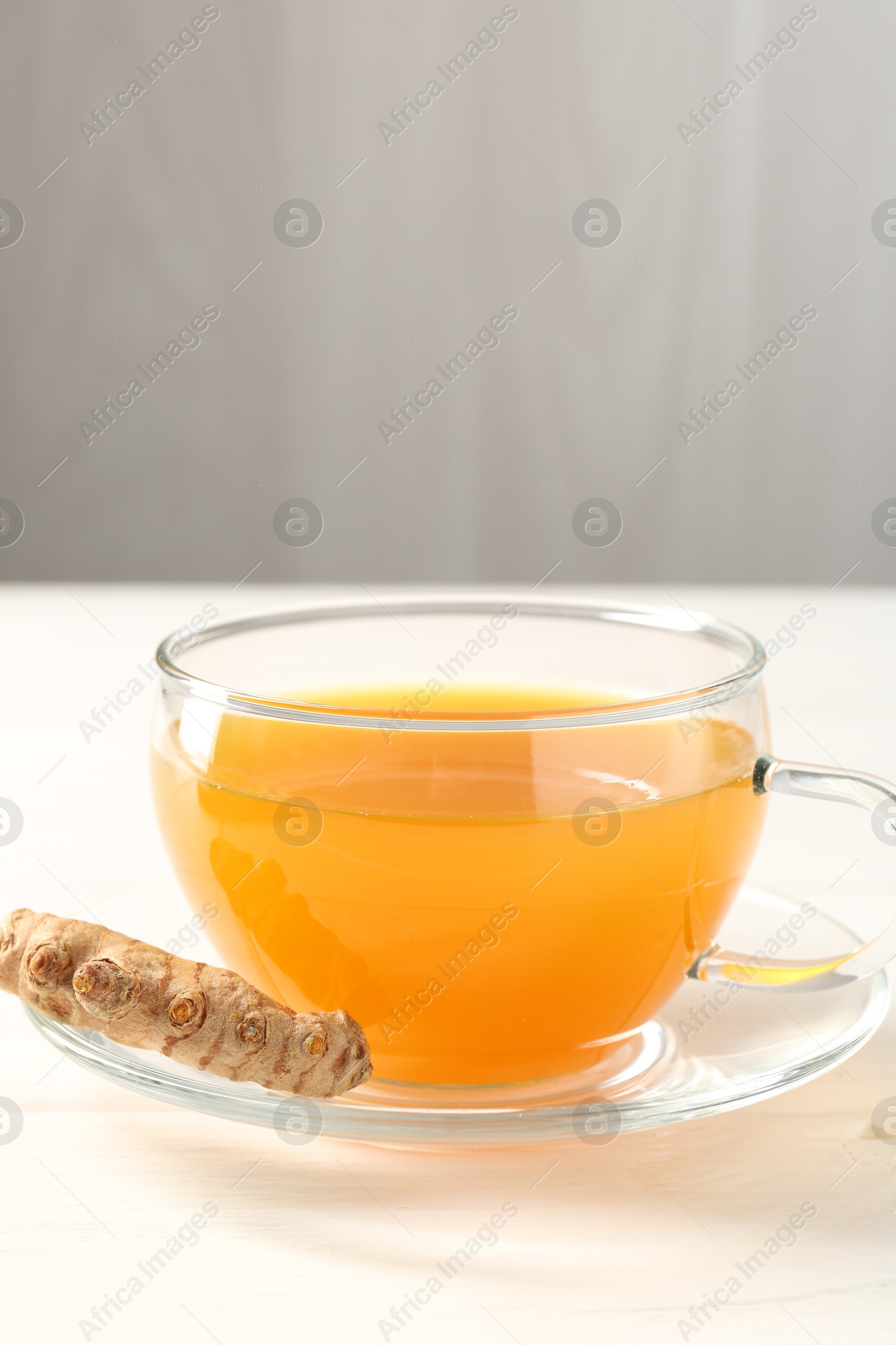 Photo of Aromatic turmeric tea in glass cup and root on white wooden table, closeup