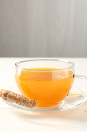 Photo of Aromatic turmeric tea in glass cup and root on white wooden table, closeup