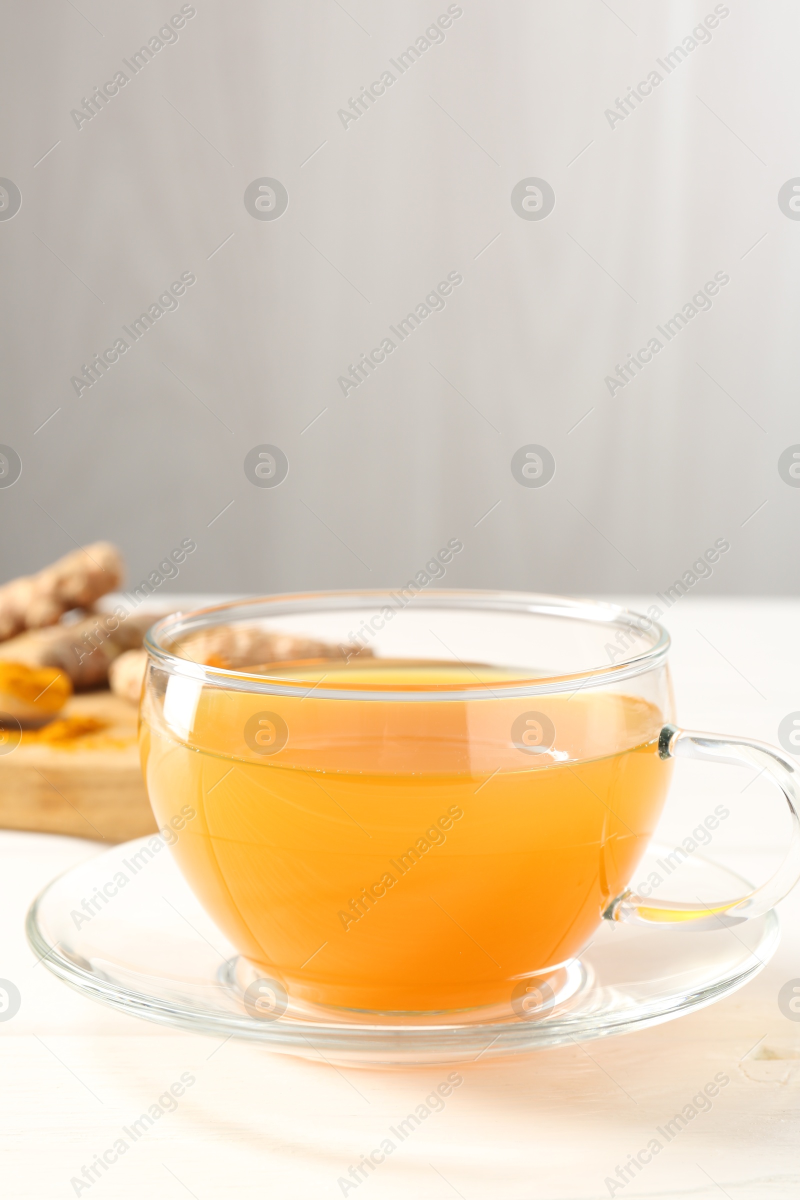 Photo of Aromatic turmeric tea in glass cup on white table, closeup