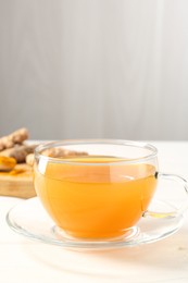 Photo of Aromatic turmeric tea in glass cup on white table, closeup