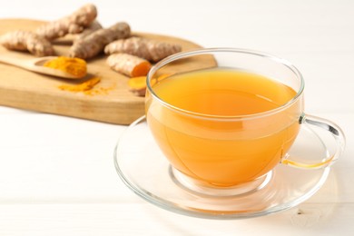 Photo of Aromatic turmeric tea in glass cup, roots and powder on white wooden table, closeup