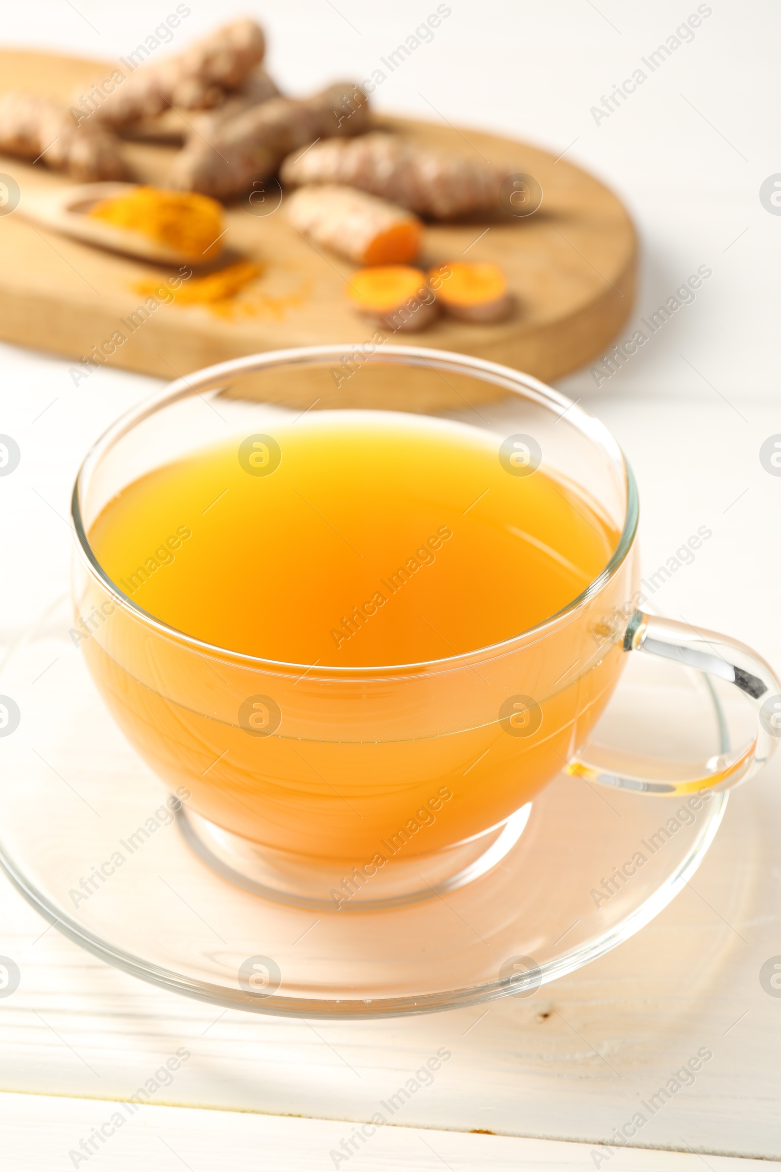 Photo of Aromatic turmeric tea in glass cup, roots and powder on white wooden table, closeup