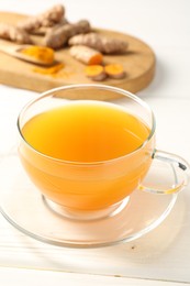 Photo of Aromatic turmeric tea in glass cup, roots and powder on white wooden table, closeup