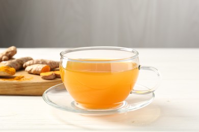 Photo of Aromatic turmeric tea in glass cup, roots and powder on white wooden table, closeup