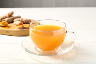 Photo of Aromatic turmeric tea in glass cup, roots and powder on white wooden table, closeup