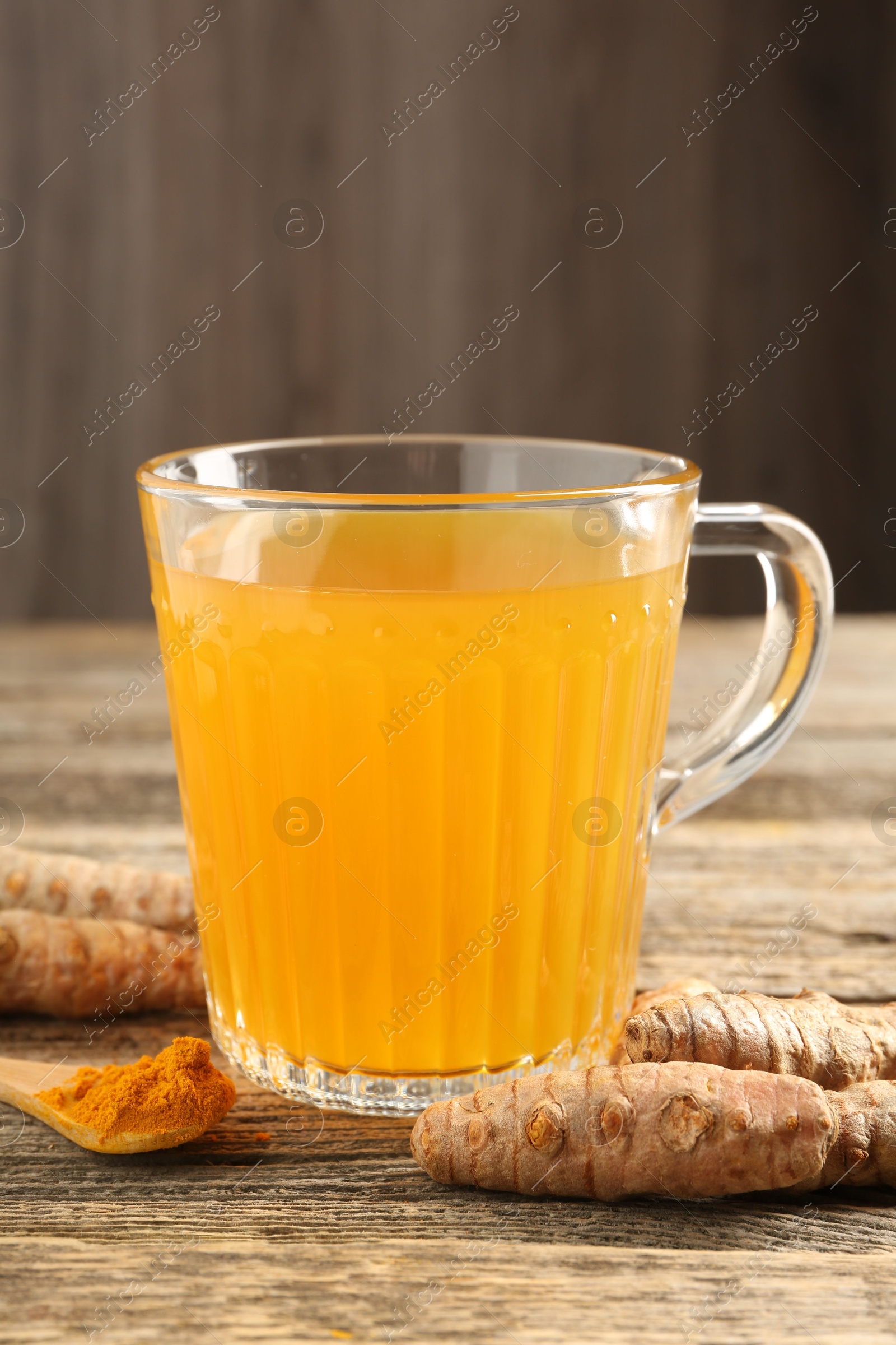 Photo of Aromatic turmeric tea in glass mug, roots and powder on wooden table, closeup