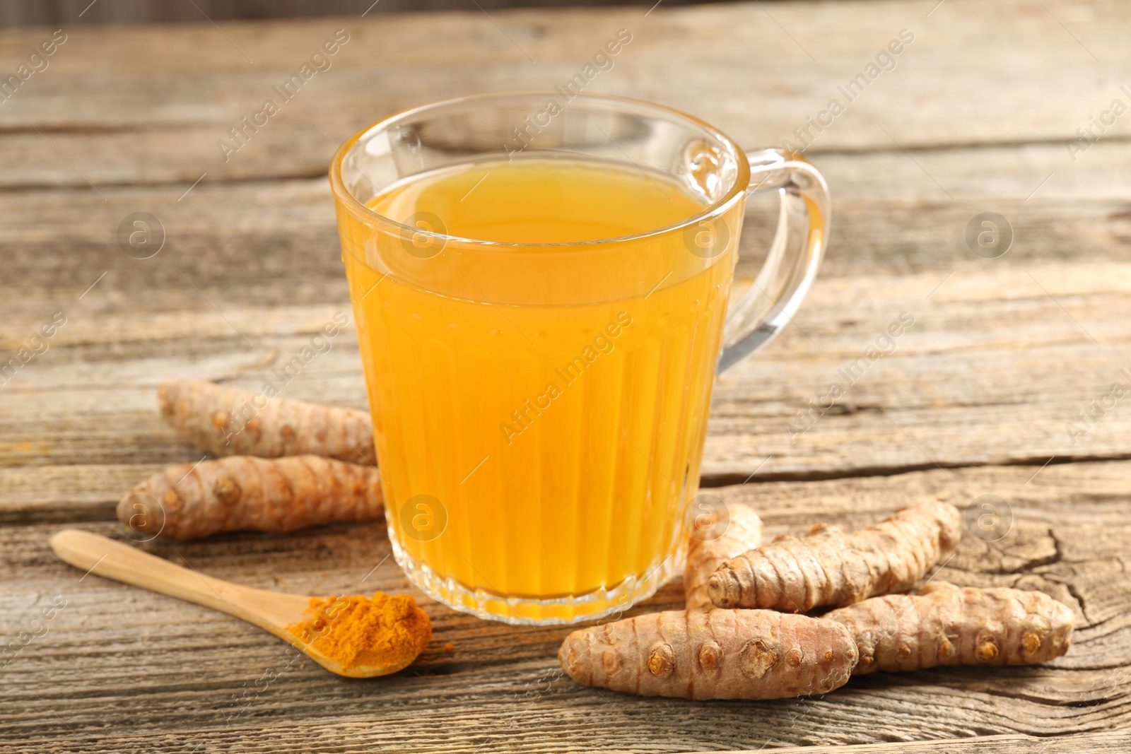 Photo of Aromatic turmeric tea in glass mug, roots and powder on wooden table, closeup