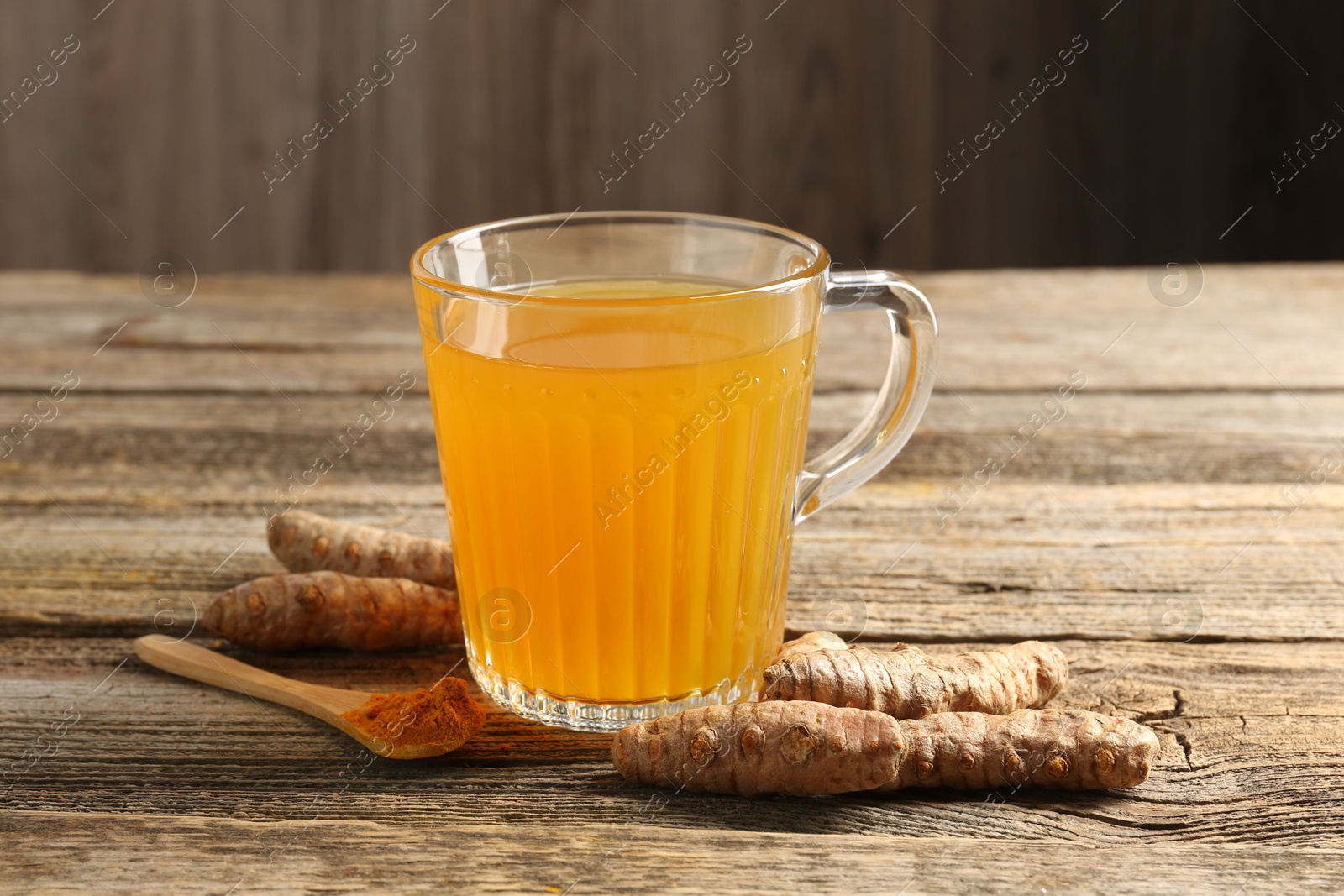 Photo of Aromatic turmeric tea in glass mug, roots and powder on wooden table