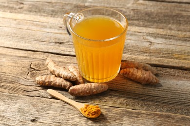 Photo of Aromatic turmeric tea in glass mug, roots and powder on wooden table, closeup