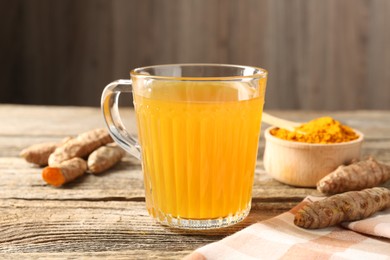 Photo of Aromatic turmeric tea in glass mug, roots and powder on wooden table, closeup