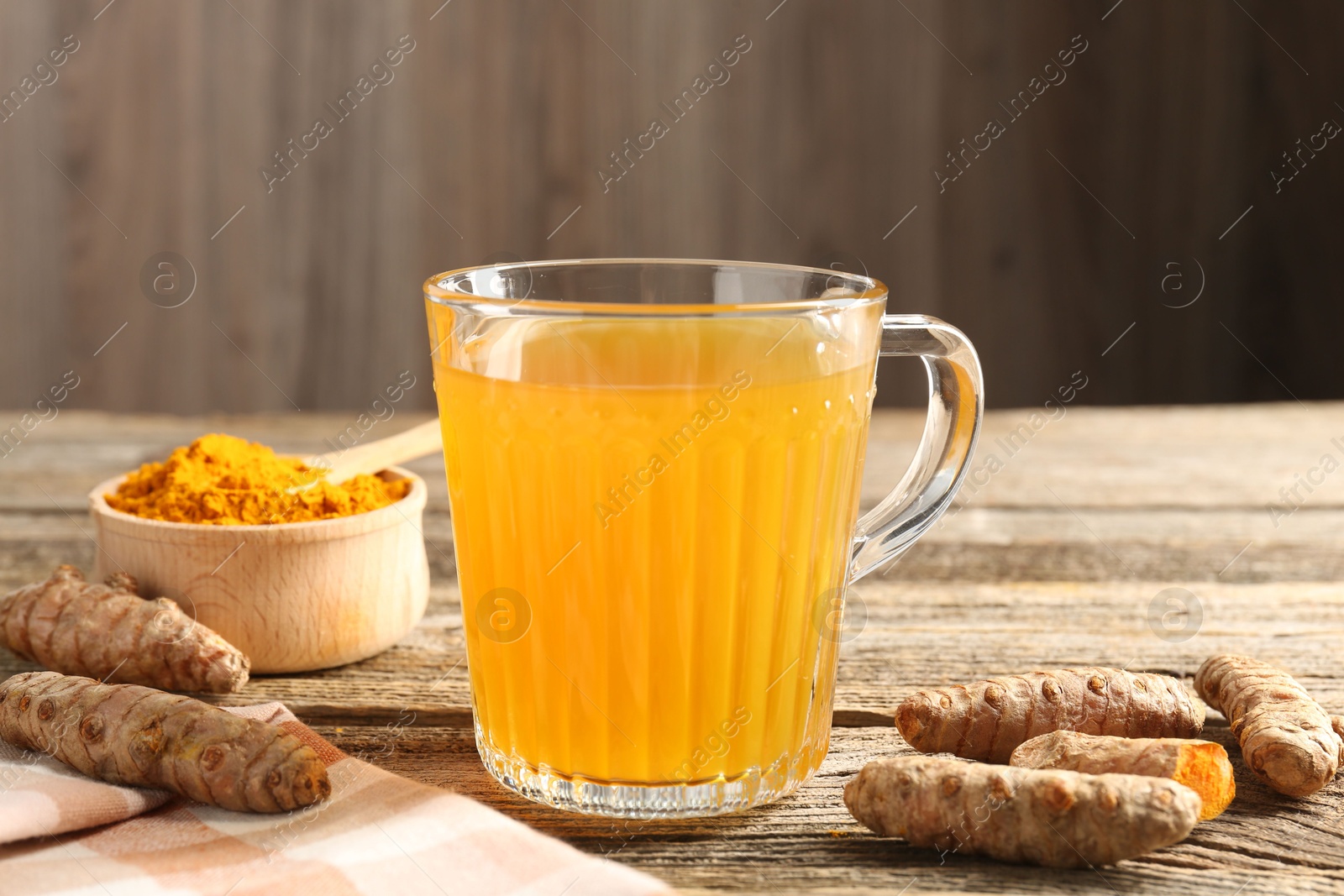 Photo of Aromatic turmeric tea in glass mug, roots and powder on wooden table, closeup